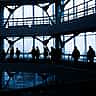 Silhouettes of people walking along the elevated walkways of a modern, multi-level glass office building.