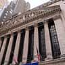 The classic stone facade and columns of the New York Stock Exchange building seen from a low angle.