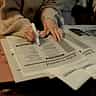 A person uses a pink marker to highlight job listings in the classifieds section of a newspaper.