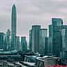 A wide, golden-hour view of the dense, modern skyline of Shenzhen with multi-lane railway tracks cutting through the city.