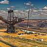 A massive bucket-wheel excavator operates in a vast open-pit mine under a cloudy sky.