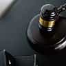 A close-up view from above of a dark wooden judge's gavel with a gold band resting on a black desk.