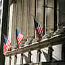 American flags hang between the sunlit columns of the New York Stock Exchange building.