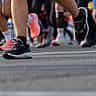 A close-up view of the feet and legs of multiple marathon runners moving along a paved road.