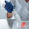A gloved researcher uses a multi-channel pipette to transfer liquid into a microplate in a laboratory.