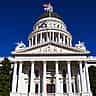 The white facade and dome of the California State Capitol building against a clear blue sky.