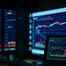 Glowing screens display fluctuating stock market charts and data in a darkened room.