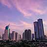 Modern skyscrapers rise into a pink and purple sunset sky in Jakarta, Indonesia.