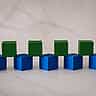 Blue and green wooden blocks arranged in an interlocking foundation pattern on a bright marble surface.