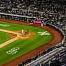 An aerial view of a baseball game underway at Yankee Stadium with the team logo visible on the field.