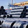 Massive stacks of steel wire coils stored outdoors at a bright industrial site.