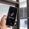A person holding a smartphone displaying the TikTok logo on the screen.