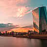 The modern glass facade of the European Central Bank headquarters in Frankfurt reflecting a vibrant sunset.