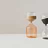 Two modern glass hourglasses with flowing sand sit side-by-side on a white surface.