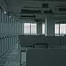 Rows of empty cubicles in a dimly lit, modern commercial office building with large glass windows overlooking a city.