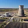 An aerial view of a nuclear power plant's cooling tower and reactor building surrounded by a field of solar panels.
