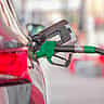 A green fuel pump nozzle fills a car at a gas station.