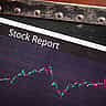 A document horizontally labeled Stock Report rests on a digital screen displaying fluctuating financial market charts.