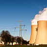 Cooling towers and high-voltage transmission lines of a power plant against a clear blue sky.