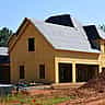 A wooden residential house with exposed framing and sheathing under construction.