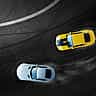 An aerial view of a yellow car and a white car drifting closely together around a curved asphalt track.