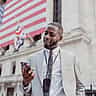 A smiling professional man looks at his smartphone while standing outside the New York Stock Exchange.