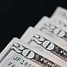 A macro shot of United States twenty-dollar bills neatly layered against a stark black background.