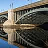 A sturdy stone and steel bridge spanning a calm river under a clear blue sky.