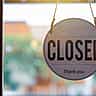 A round wooden closed sign hanging on the inside of a glass window or door.