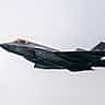 A dark gray United States Navy F-35 fighter jet flies through an overcast sky.