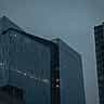 Modern glass office buildings stand under a dark, overcast evening sky.