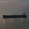A solitary oil tanker ship sailing on calm ocean waters during twilight.