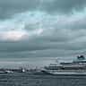 A large cruise ship anchored at port under a heavy, dramatic sky.