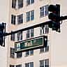 A green Wall Street street sign hangs next to a traffic light against a light-colored building facade.