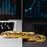 Gold Bitcoin tokens sit on a laptop keyboard in front of a screen displaying a financial chart.