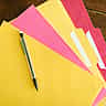 A black pen rests on a neatly fanned stack of yellow and pink file folders on a wooden desk.