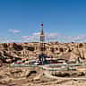 An active oil drilling rig surrounded by facilities in a vast, arid, rocky desert landscape.