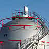 A large, spherical industrial natural gas storage tank with a metal staircase winding around it against a blue sky.