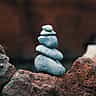 A stack of smooth, blue-grey stones carefully balanced on a textured red rock.