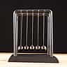 A metal Newton's cradle resting on a wooden surface against a dark background.