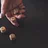 A hand rolling three wooden dice onto a dark surface in moody, dramatic lighting.