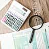 A magnifying glass and a calculator resting on top of U.S. individual income tax forms on a wooden desk.