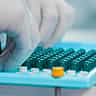 Gloved hands carefully arranging green pharmaceutical capsules in a bright, modern laboratory setting.