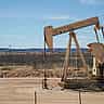 An active oil pumpjack operates in a dry, sunlit landscape under a clear blue sky.