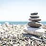 Smooth stones of varying sizes are carefully balanced in a vertical stack on a bright pebble beach.
