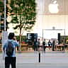 A glowing Apple logo above the glass facade of a modern retail store surrounded by trees.