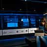 A woman works on a laptop in a server room behind a glass wall displaying the logos of various technology companies.