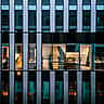 An illuminated, empty modern office space seen through the glass facade of a commercial building at night.