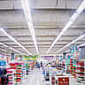 A wide, brightly lit interior of a large modern supermarket with stocked shelves and department signs.