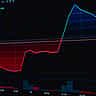 A dark computer screen displays a financial candlestick chart with a steep downward trend of red bars.